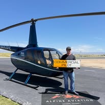 New commercial pilot holding the sign by the helicopter